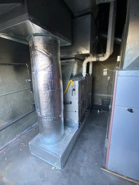 Insulated HVAC ductwork with reflective wrap and metal piping in commercial mechanical room