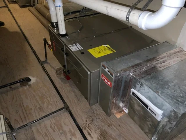 New furnace unit with white PVC ductwork and piping in mechanical room