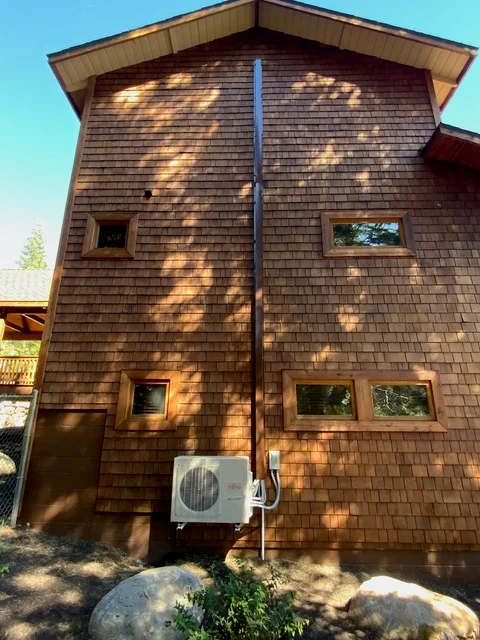 Mini-split heat pump unit installed on cedar shake exterior wall with refrigerant lines
