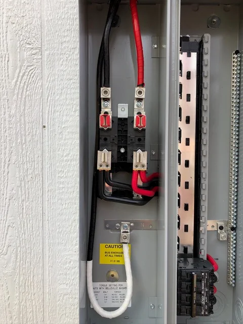 Electrical disconnect panel with red-handled breakers, power cables, and safety caution label on white textured wall
