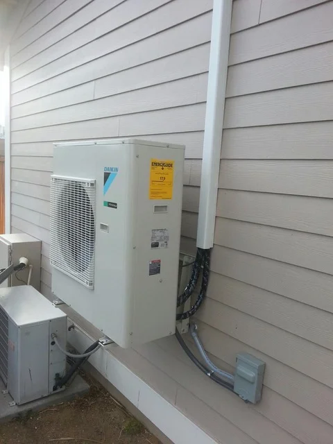 Heat pump condenser unit installed on concrete pad with refrigerant lines and electrical connections