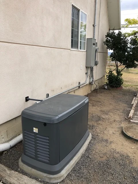 Gray standby generator unit on concrete pad beside residential building with conduit connections