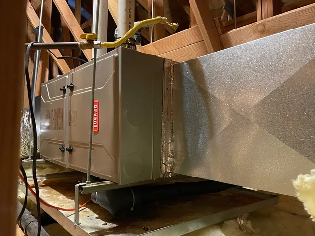 Furnace unit installed in attic with wooden framing, metal ductwork, and refrigerant lines