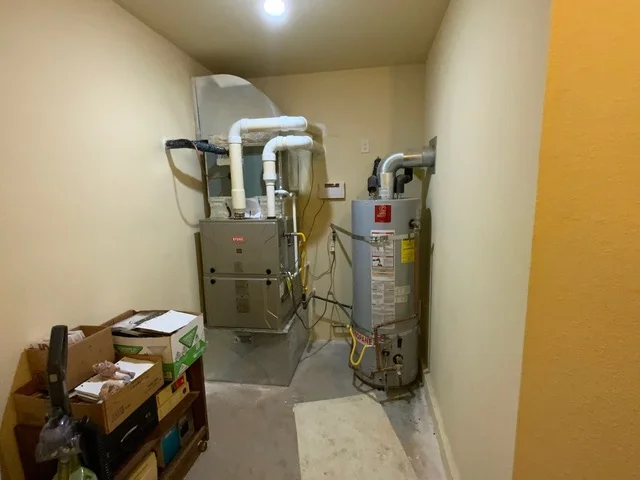 Installed furnace and water heater with white ductwork and electrical connections in utility room