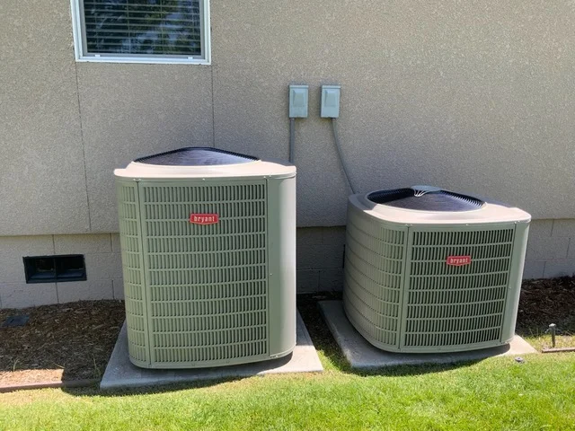 Two beige AC condenser units on concrete pads with electrical conduit connections