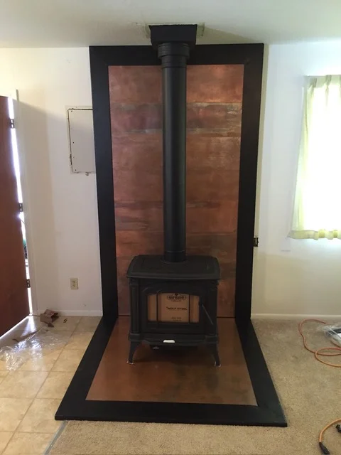 Black steel frame wood stove surround with copper heat shield and base platform