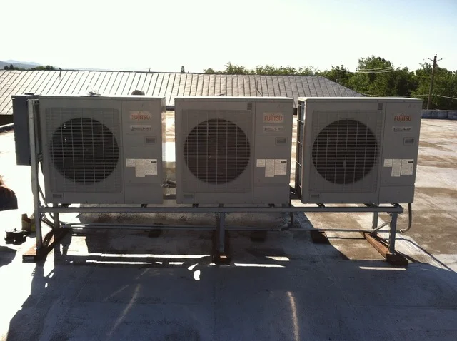 Three commercial HVAC condenser units with fan coils mounted on rooftop metal support frame