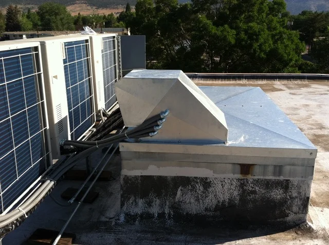 Commercial rooftop HVAC units with white metal casings and black ductwork on concrete pad